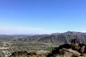 Panoramic view of Coachella Valley taken from South Lykken Trail with two hikers posing on ridge trail.